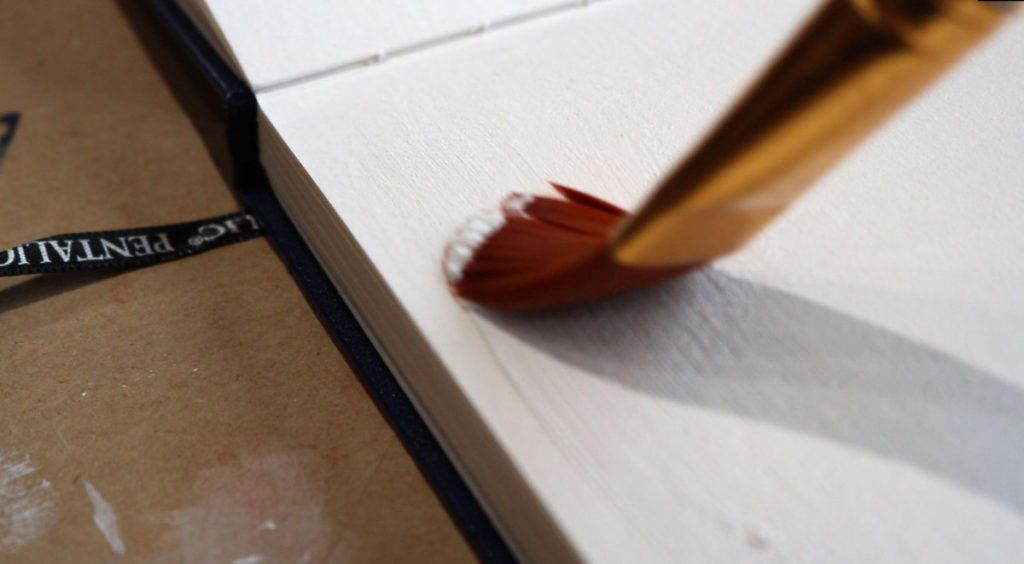 artists brush painting on the corner of a hardbound sketchbook